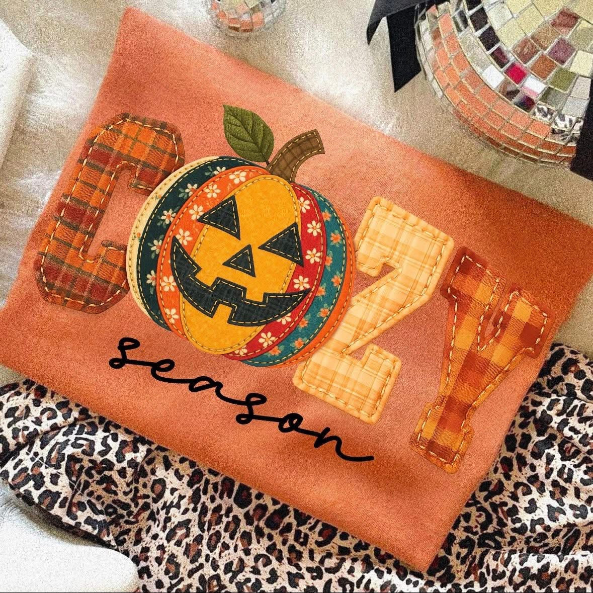 t-shirt with a fall graphic that says βCozy Season,β featuring a plaid patchwork pumpkin jack-oβ-lantern design.