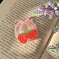 Strawberry-shaped hair tie with pink bow on an open book with purple flowers.