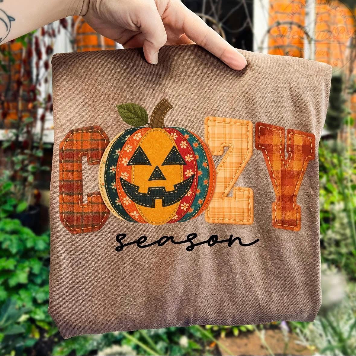 t-shirt with a fall graphic that says ‘Cozy Season,’ featuring a plaid patchwork pumpkin jack-o’-lantern design