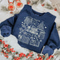 sweatshirt with a white holiday book-themed design and the phrase ‘All Booked for Christmas,’ styled flat lay with festive decor including pine branches, red berries, and cozy reindeer slippers.