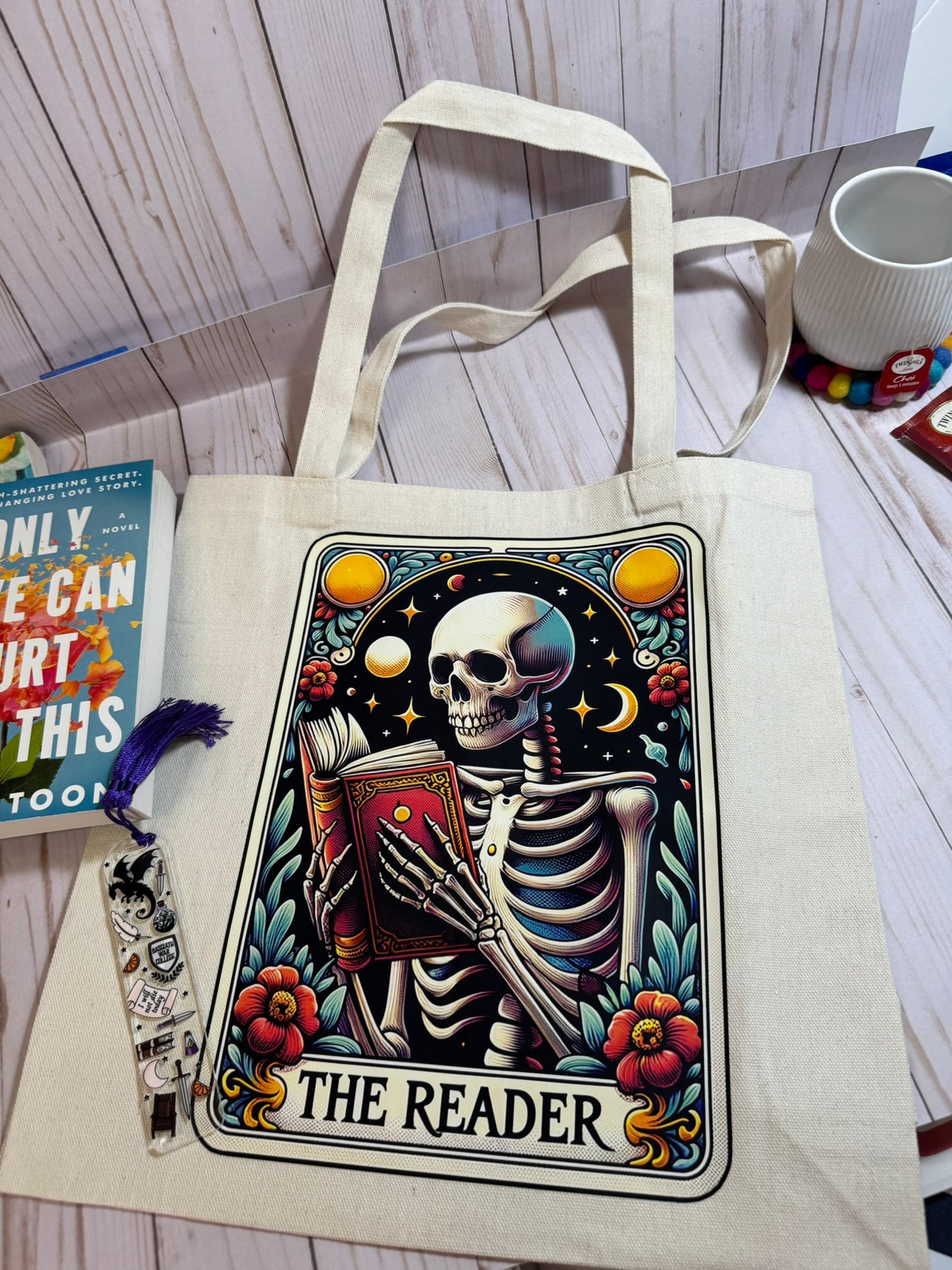 Tote bag with a skeleton design titled 'The Reader' on a wooden surface.