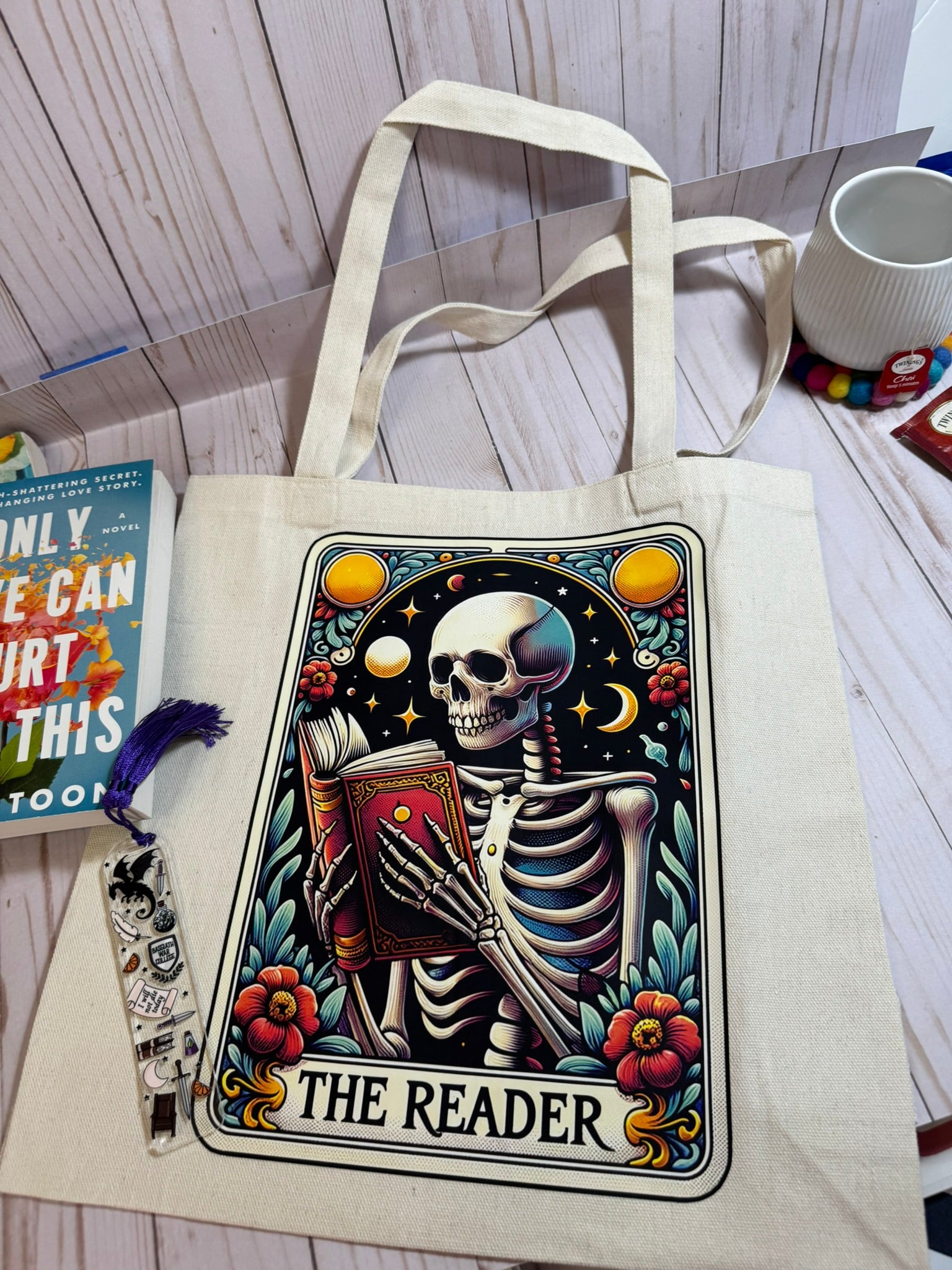 Tote bag with a skeleton design titled 'The Reader' on a wooden surface.
