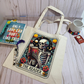 Tote bag with a skeleton design labeled 'The Reader' on a wooden surface with a book and mug.