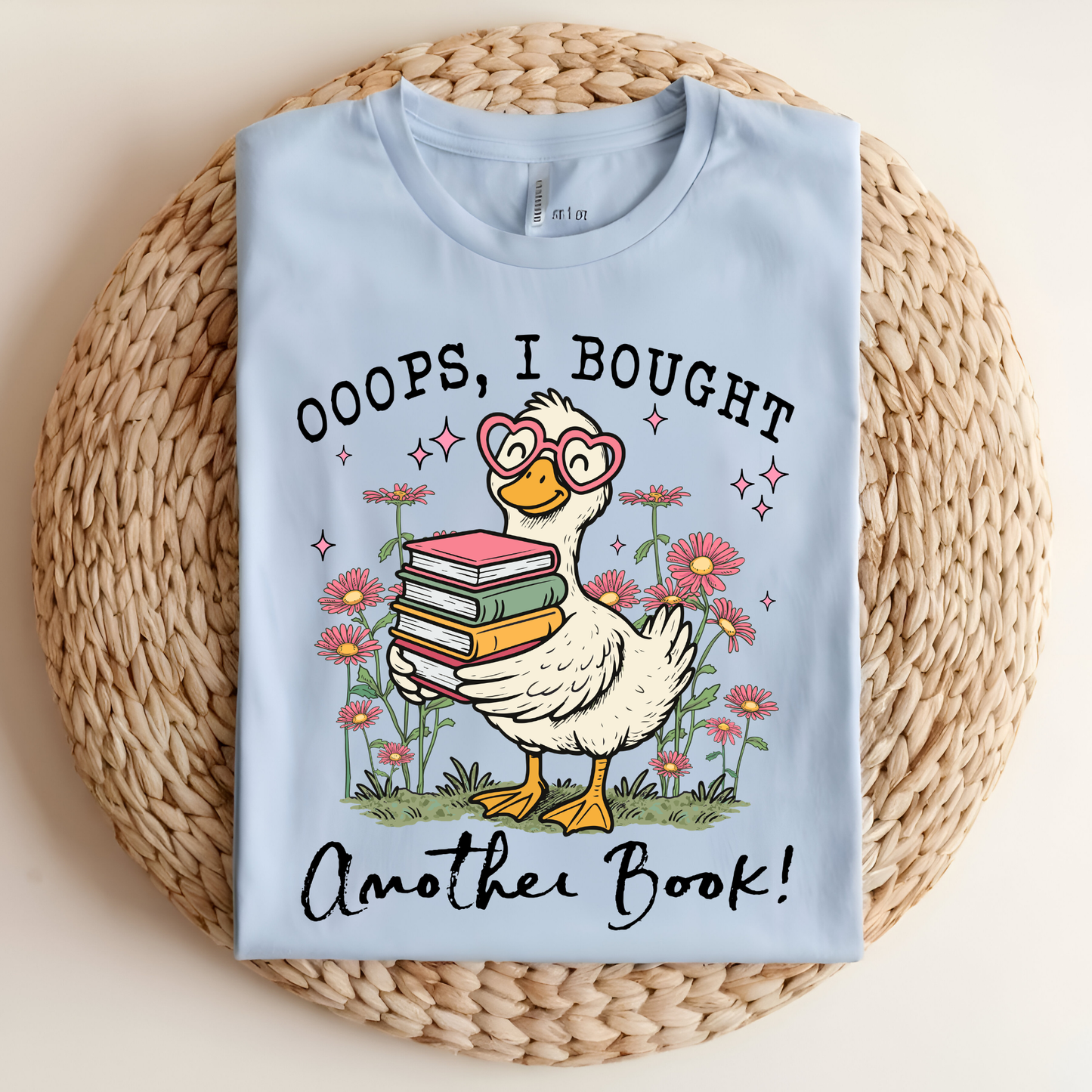 Light blue t-shirt with a cartoon duck holding books and text on a woven mat
