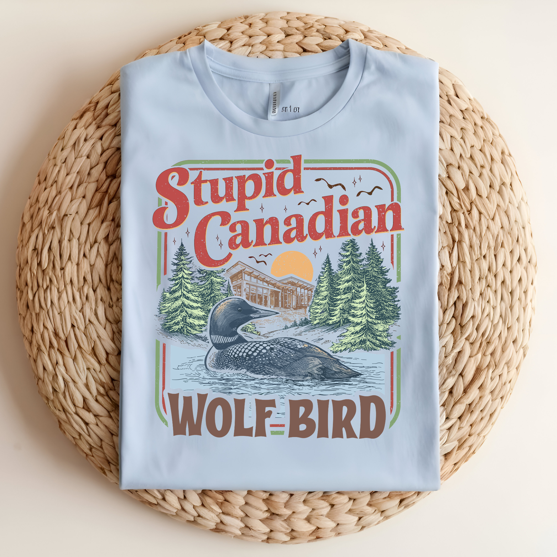 Light blue t-shirt with 'Stupid Canadian Wolf Bird' graphic on a woven mat